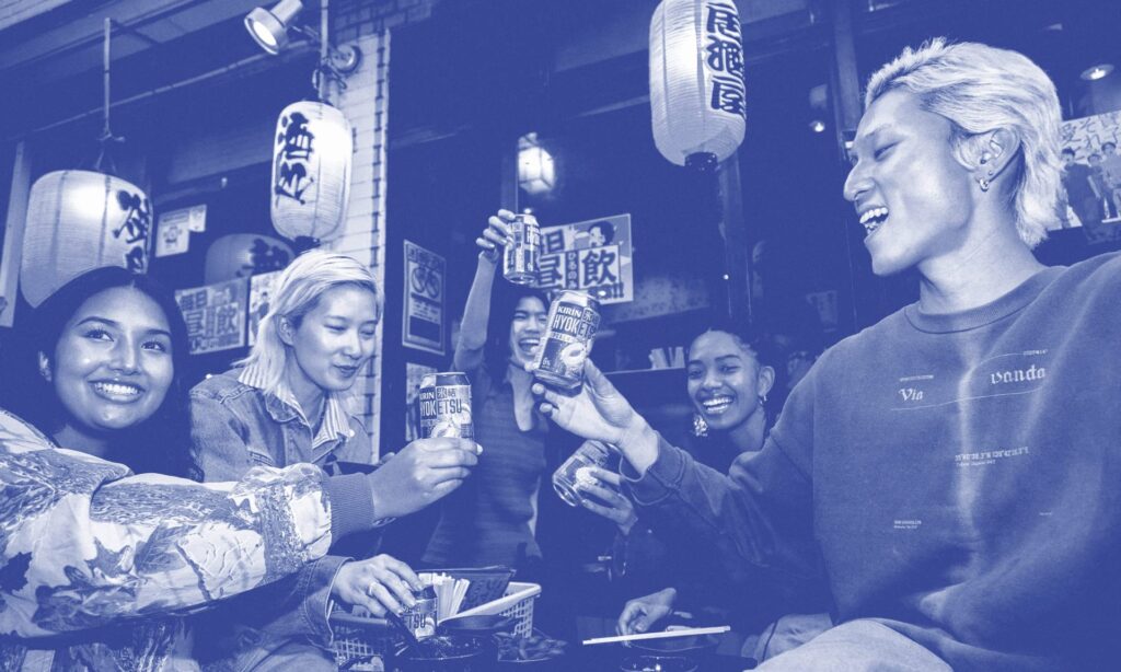 A group of cool looking friends smiling and laughing as the enjoy cans of Kirin Hyoketsu as they toast in a Japanese izakaya
