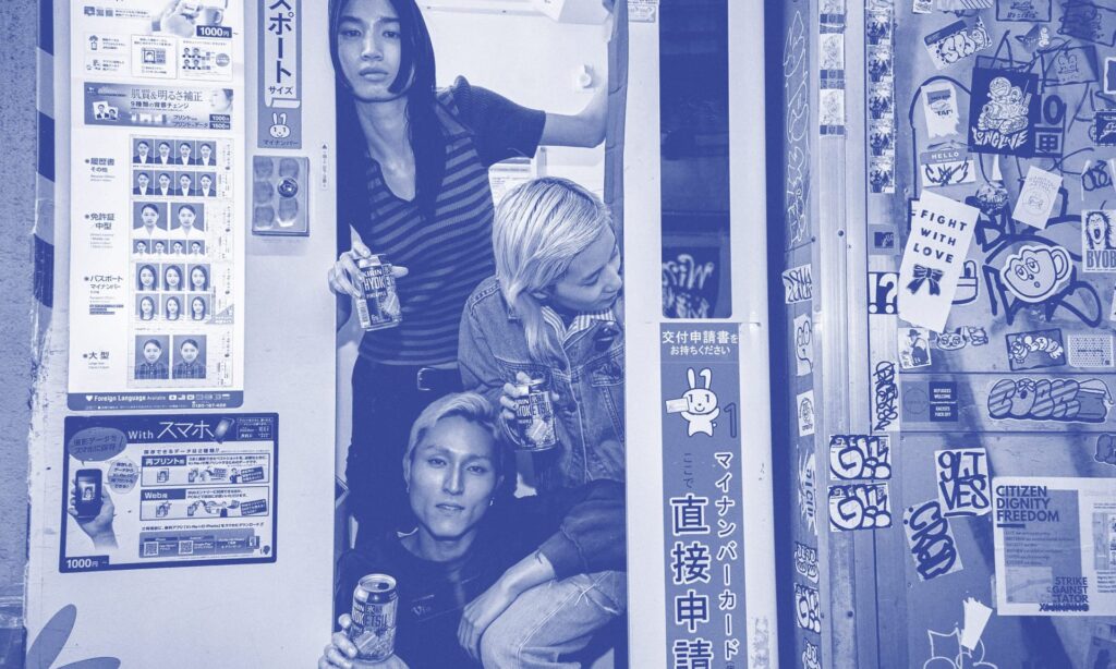 A group of cool looking friends smiling and laughing as the enjoy cans of Kirin Hyoketsu as they have fun in a photo-booth on the street